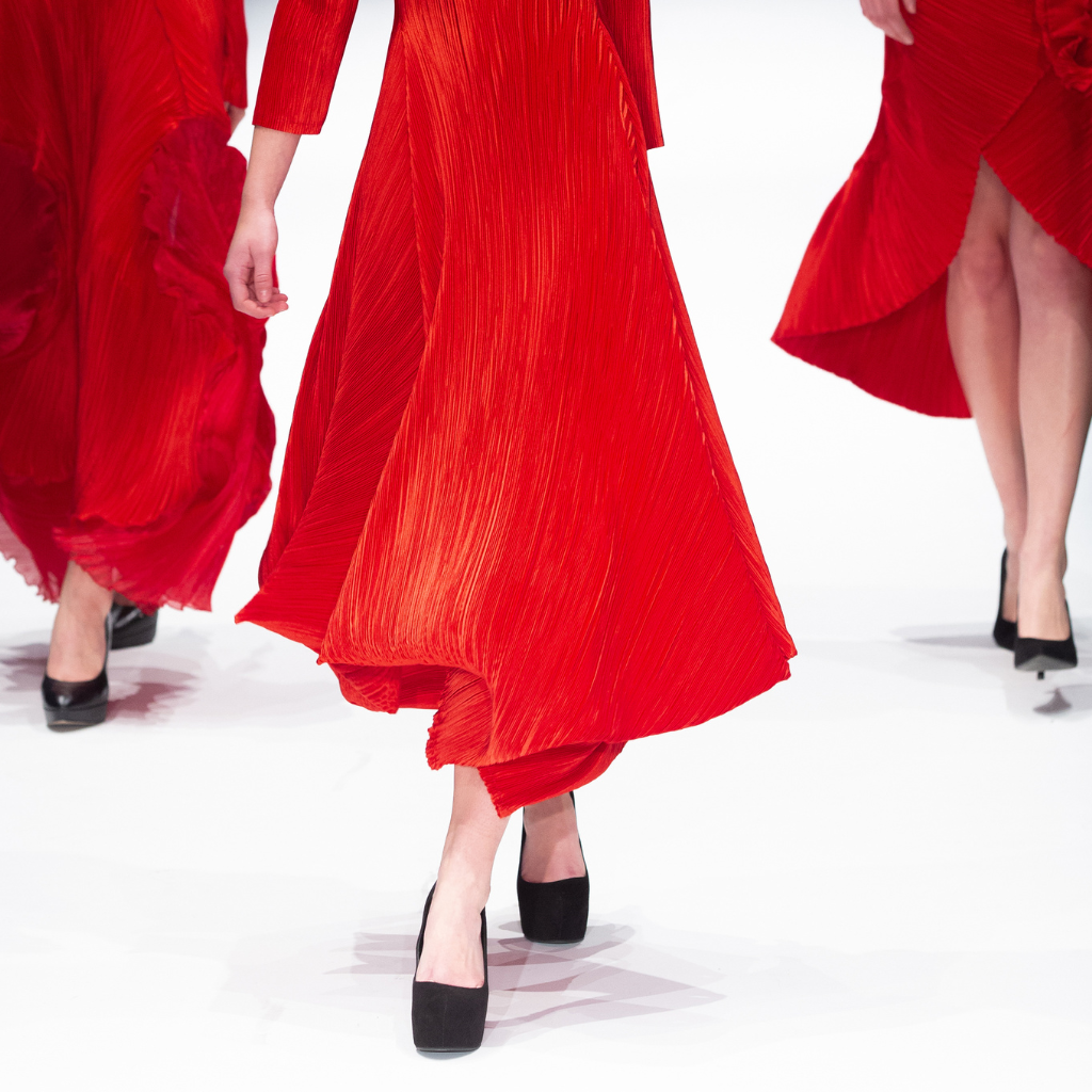 3 female models steps in red dresses and black heels walking the Runway