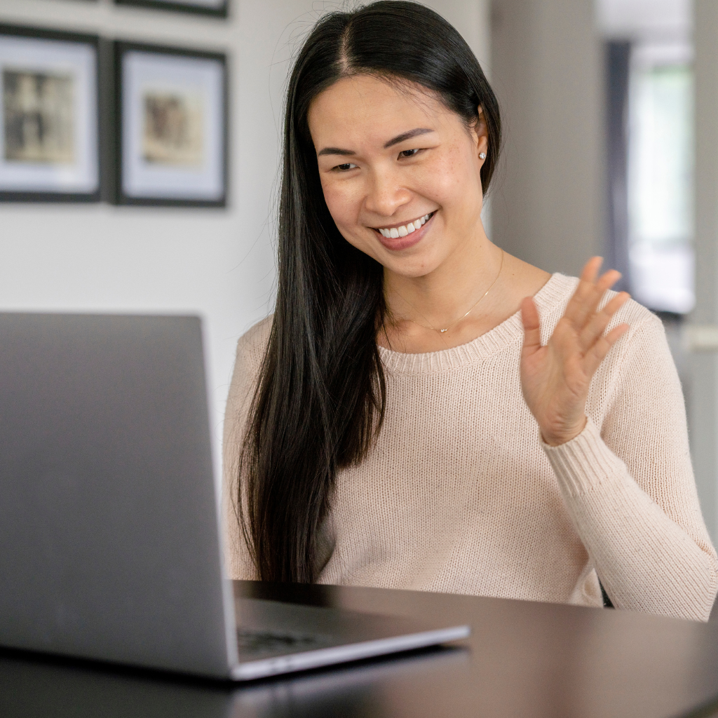 Woman waving to laptop webcam for her virtual Zoom audition.