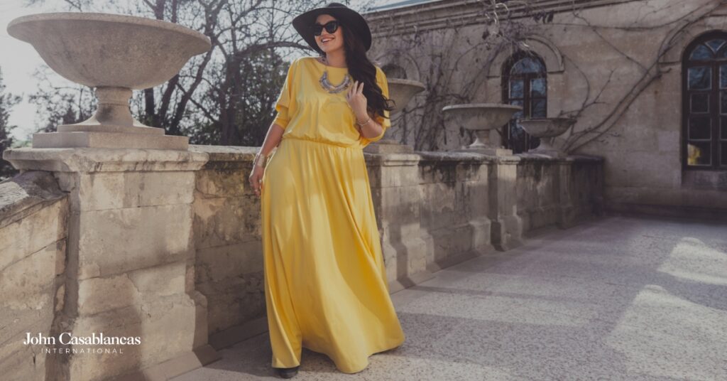 a curve model posing in a yellow dress and a black hat