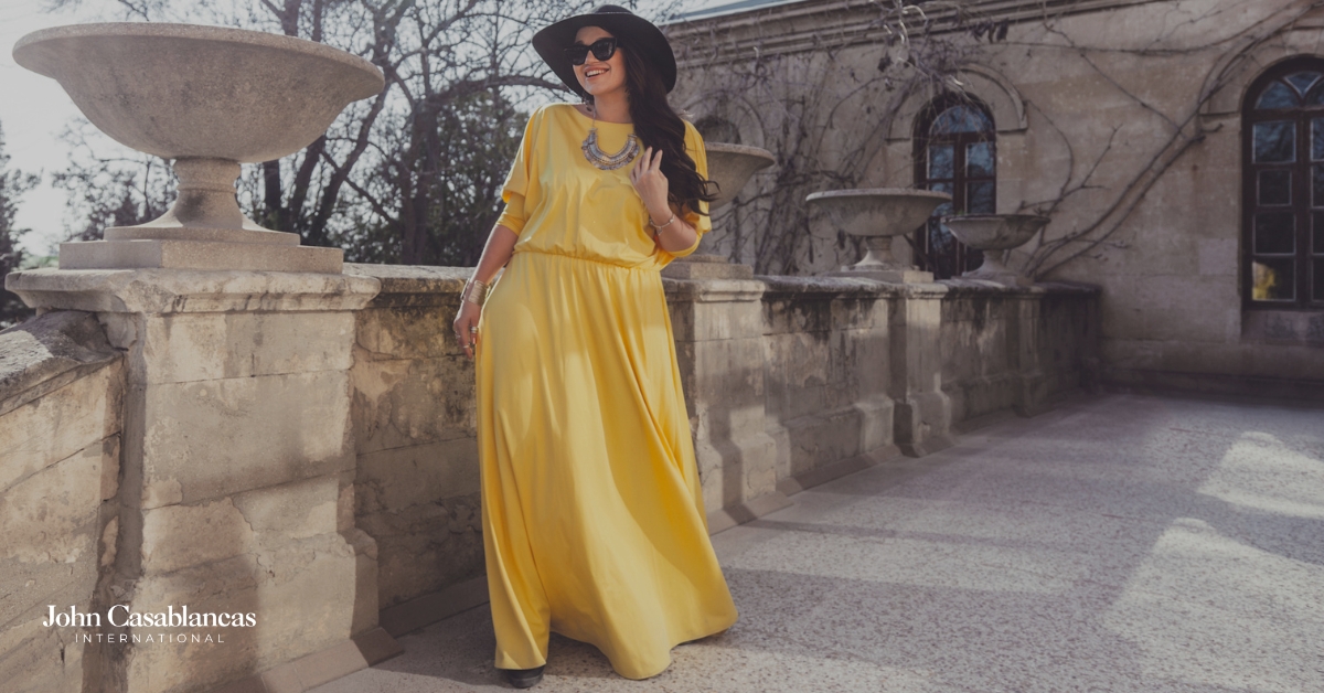 a curve model posing in a yellow dress and a black hat